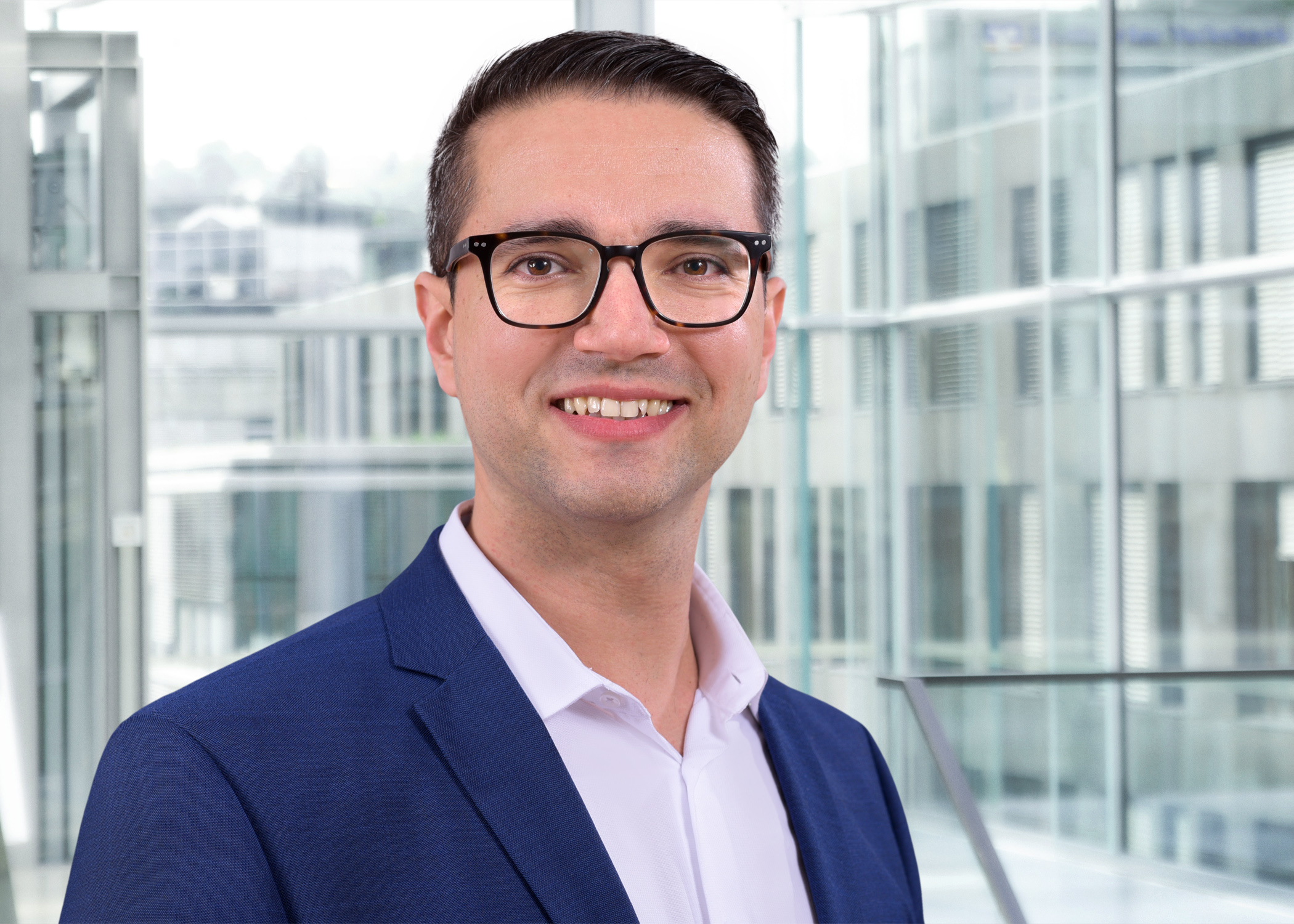 Porträt von Dr.-Ing. Tobias Reinhardt, Wasserwirtschaftsexperte im Anzug, vor moderner Glasfassade.